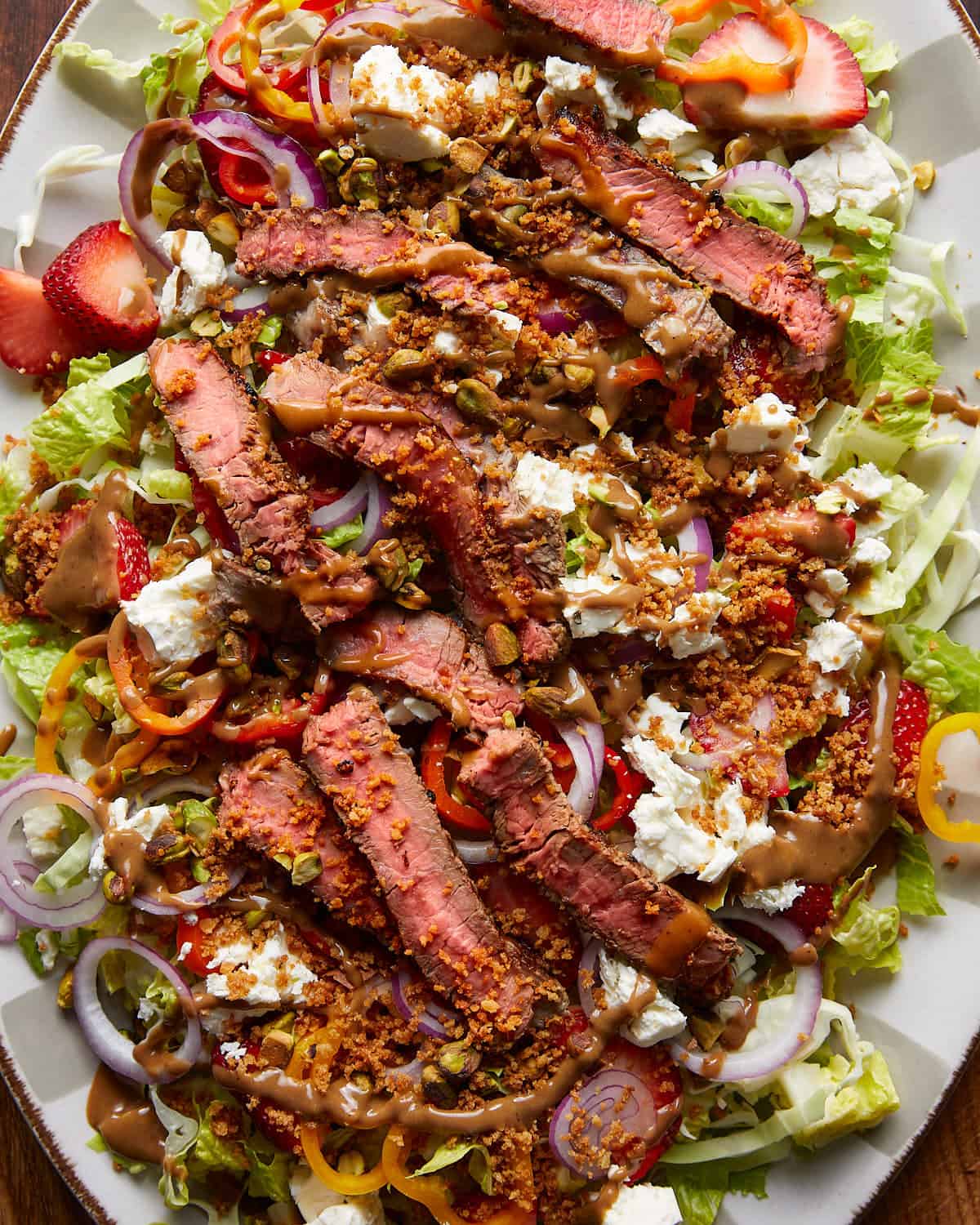 Overhead, up close image of steak salad with garnish on white platter. 