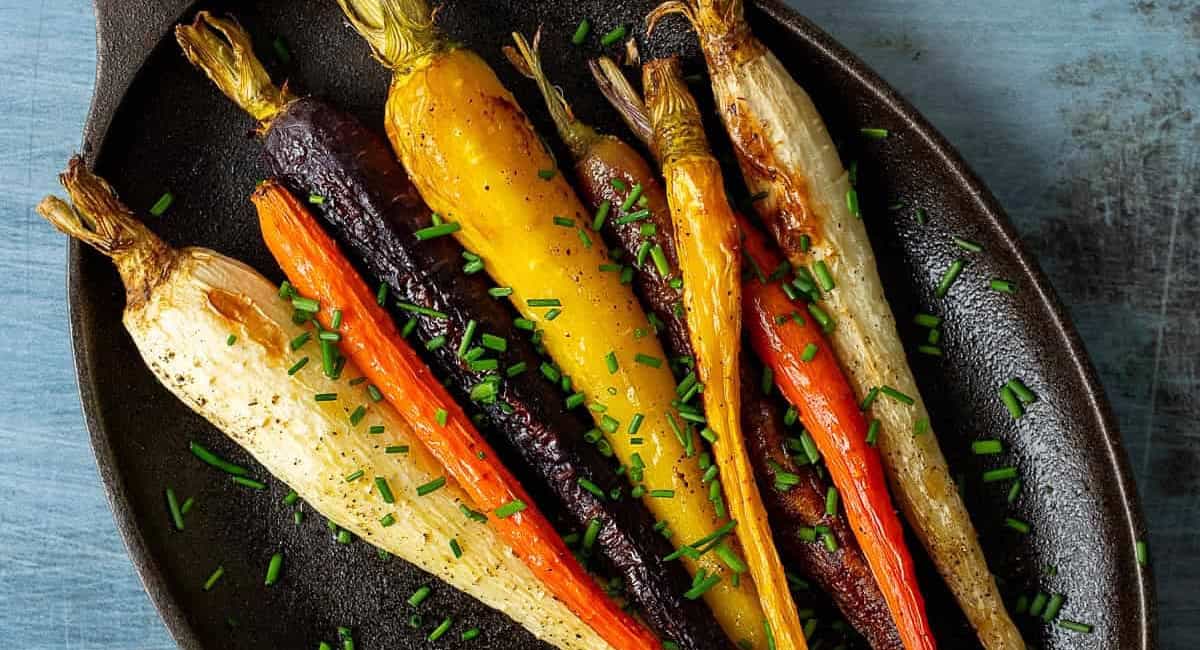 Overhead image of roasted rainbow carrots with garnish on black plate. 