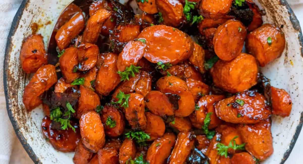 Overhead up close image of maple ginger glazed carrots with garnish in white bowl. 