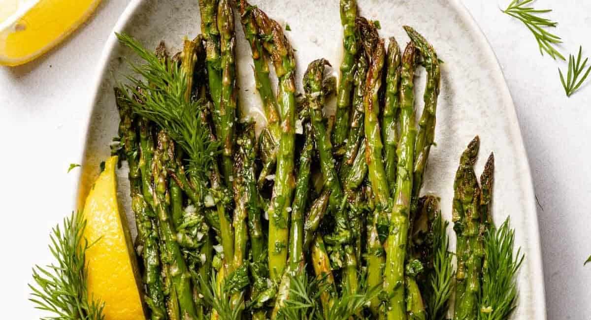 Overhead image of lemon herb roasted asparagus on white platter with garnish and lemon wedge. 