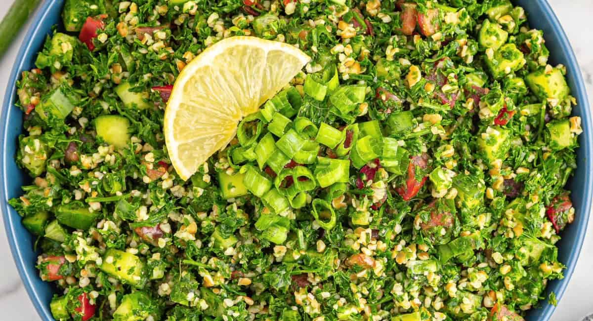 Overhead image of tabbouleg salad with lemon wedge in blue bowl. 