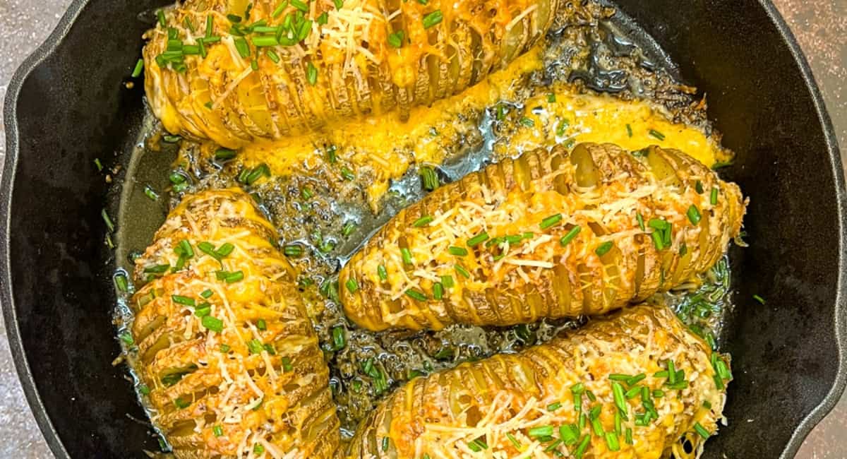 Overhead image of cheesy hasselback potatoes with garnish. 