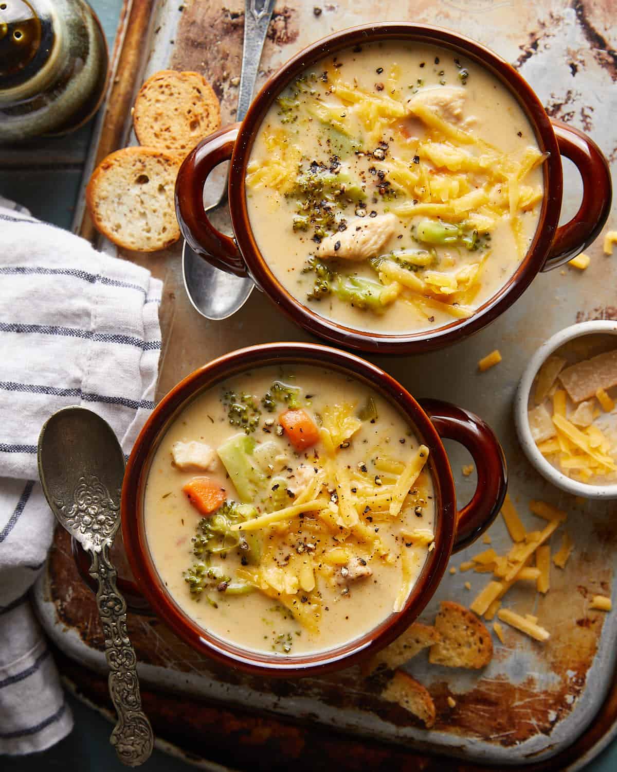 Overhead image of chicken broccoli cheddar soup in two brown soup bowls with garnish.