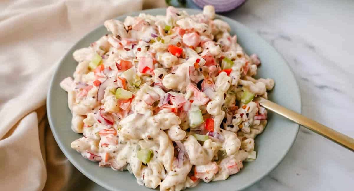 Up close image of macaroni salad on blue dish with golden spoon. 