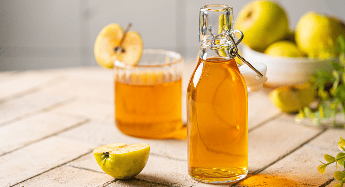 Up close image of apple cider vinegar in glass and glass bottle. 