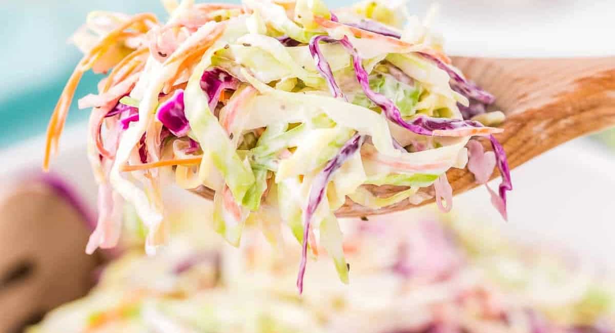 Up close image of creamy coleslaw on wooden spoon. 