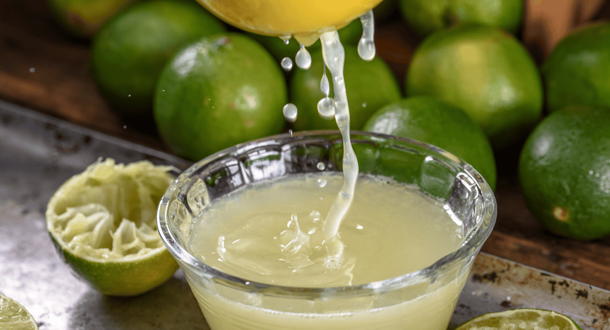Up close photo of limes being squeezed into small glass container. 