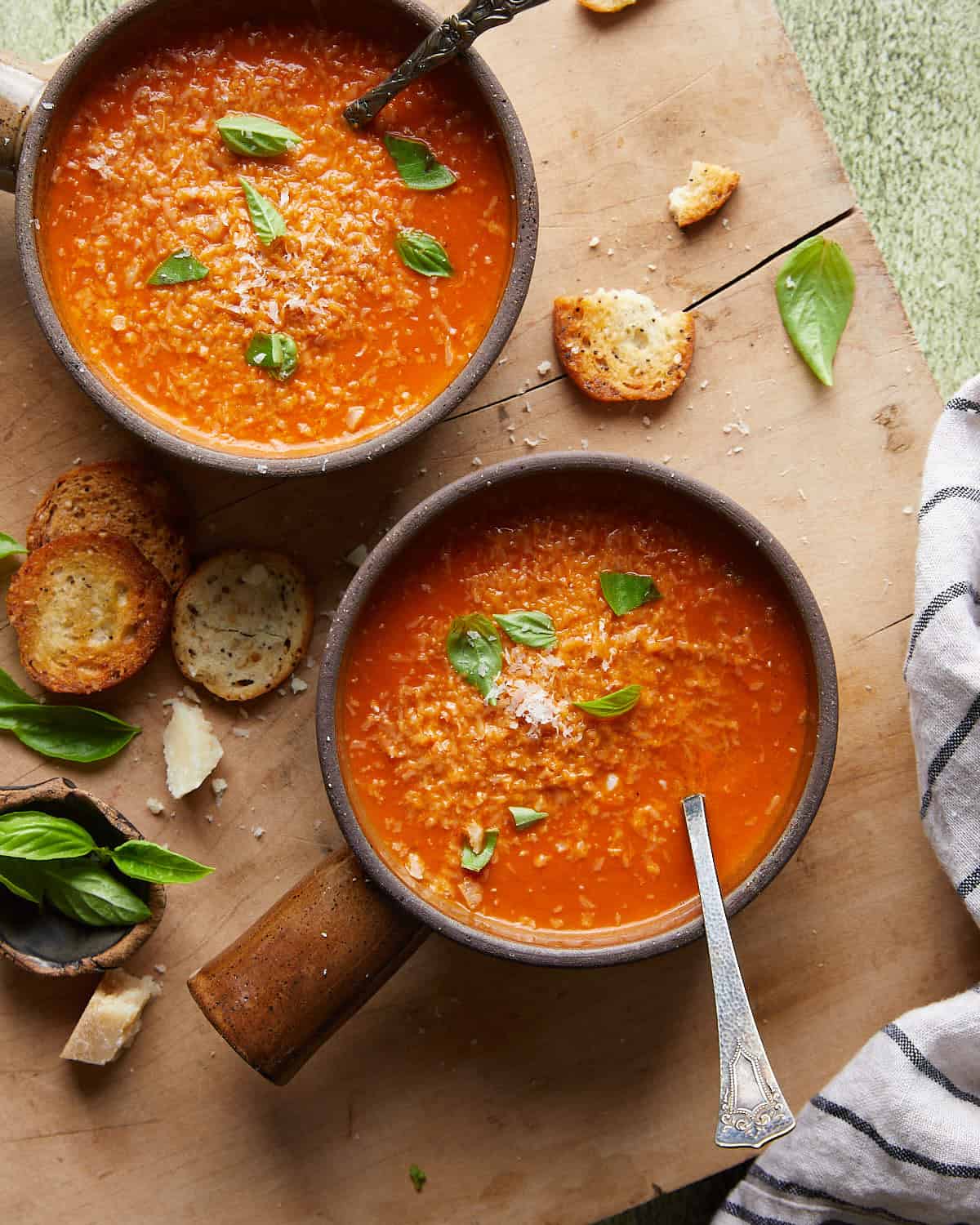Overhead image of creamy tomato basil soup in two soup bowls with garnish.