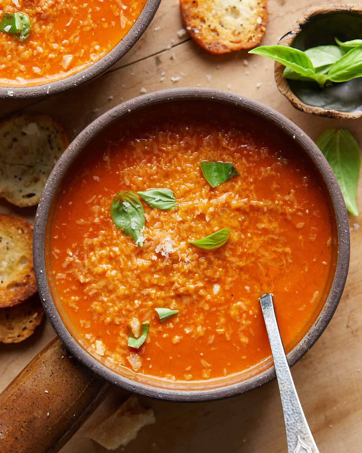 Up close overhead image of creamy tomato basil soup in soup bowl with garnish.