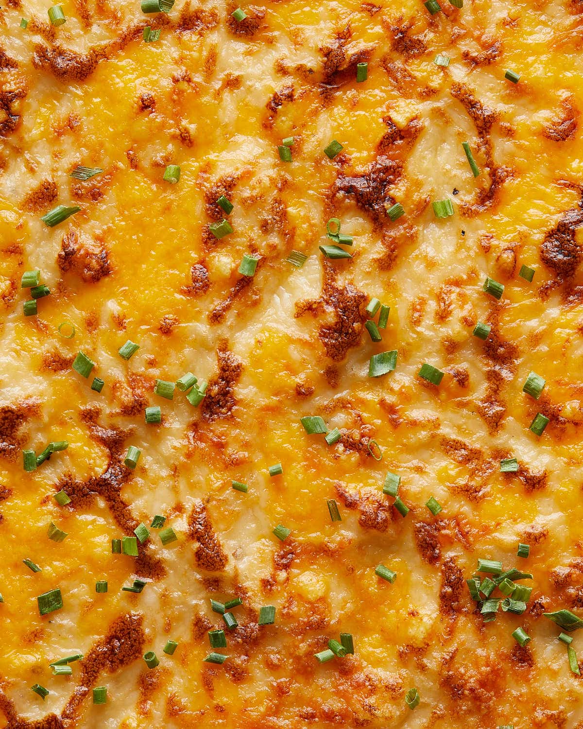 Up close and overhead image of cheesy mashed potatoes with garnish.