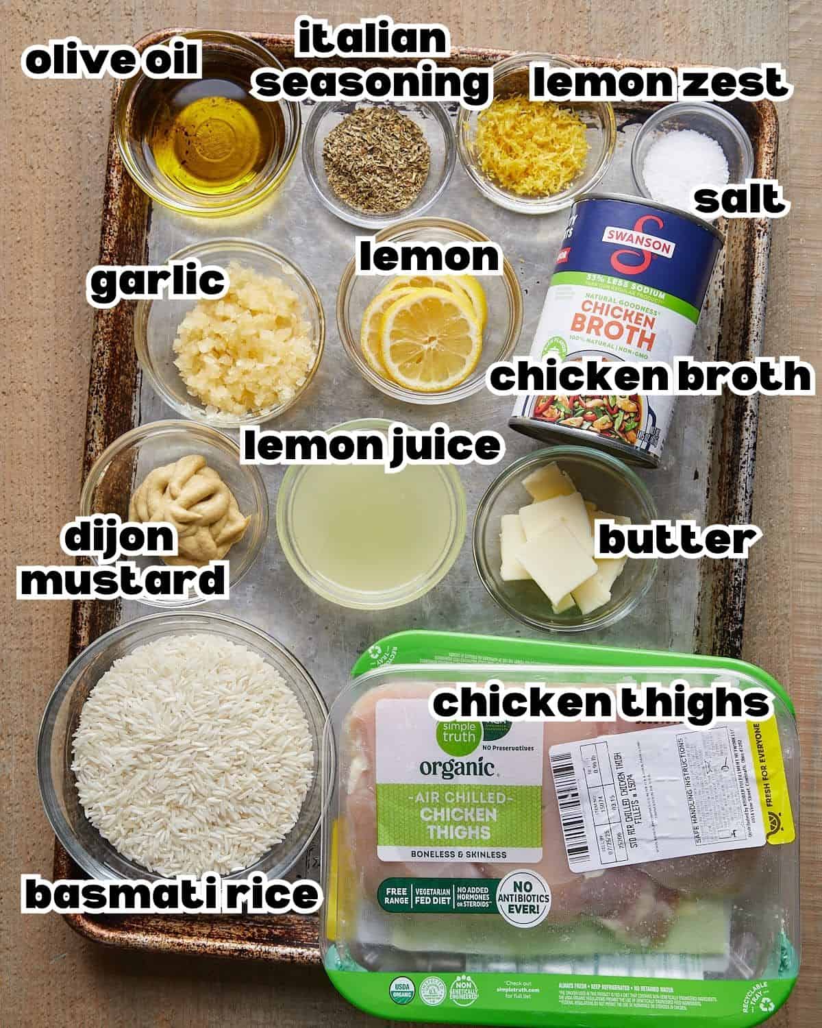 Overhead image of ingredients needed to make baked lemon chicken and rice on baking sheet.