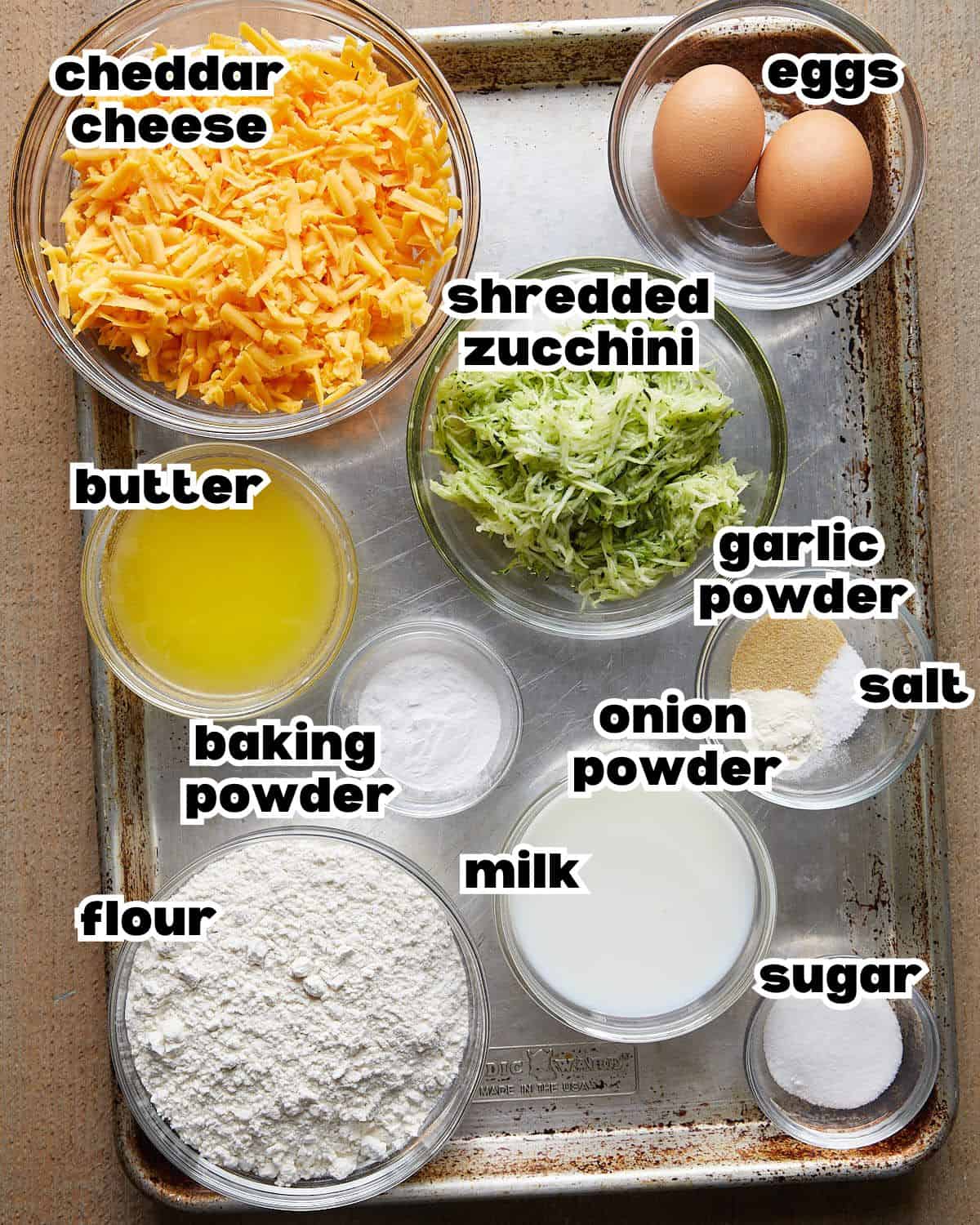 Overhead image of ingredients needed to make savory zucchini muffins on baking sheet.
