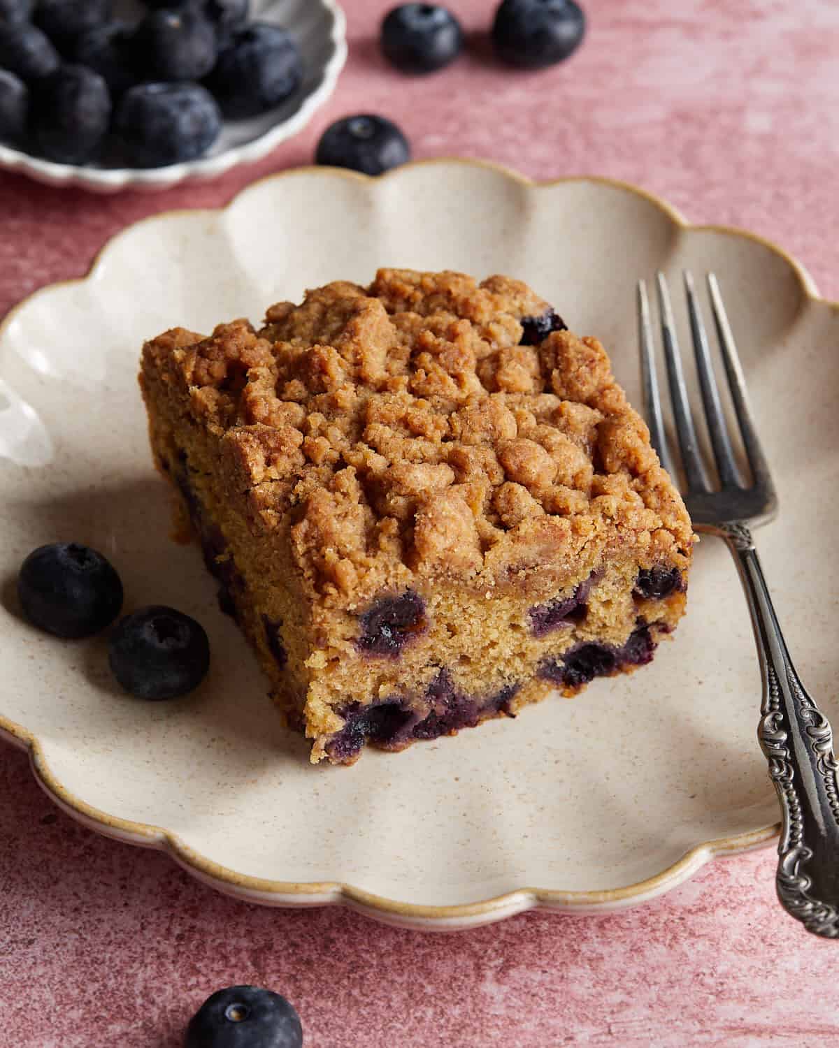 Overhead image of blueberry coffee cake on white dish with fork. 