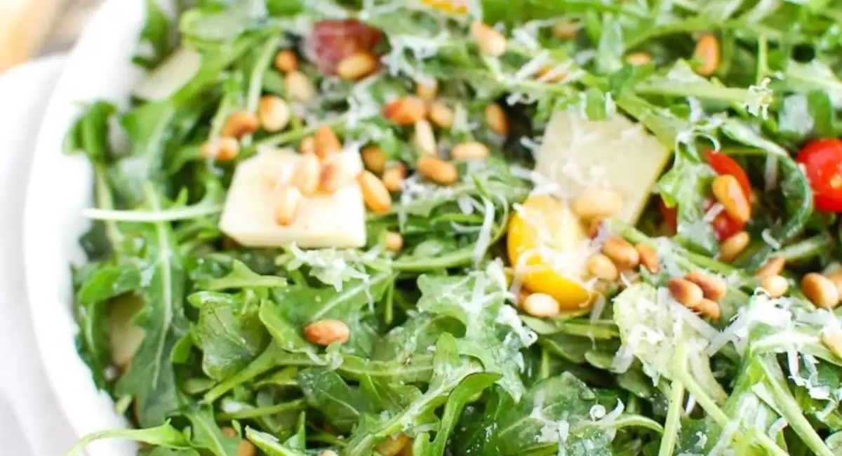 Overhead up close image of lemon arugula salad with parmesan cheese in white dish. 