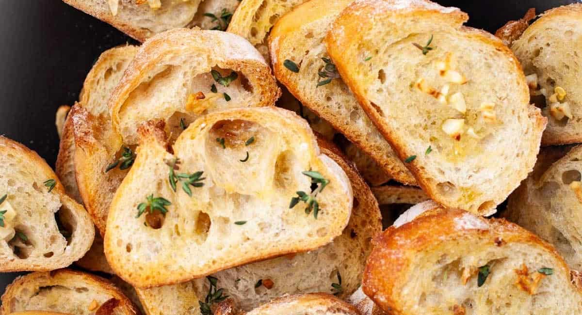 Overhead up close image of garlic crostini with olive oil and garnish. 