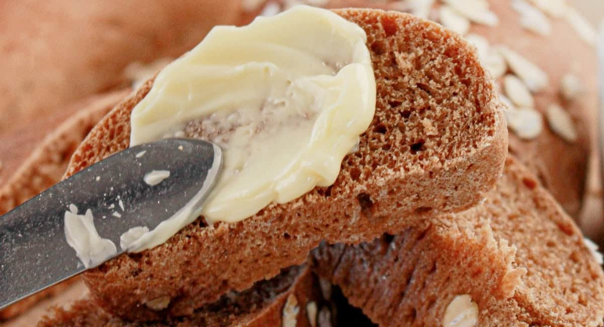 Up close image of brown bread with butter being spread with butter knife. 