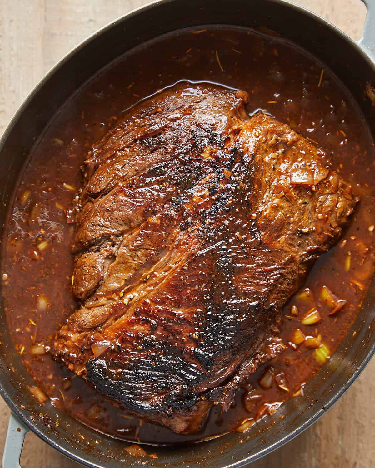 Overhead view of chuck roast added to the pot with broth and seasonings for Dutch Oven Pot Roast.