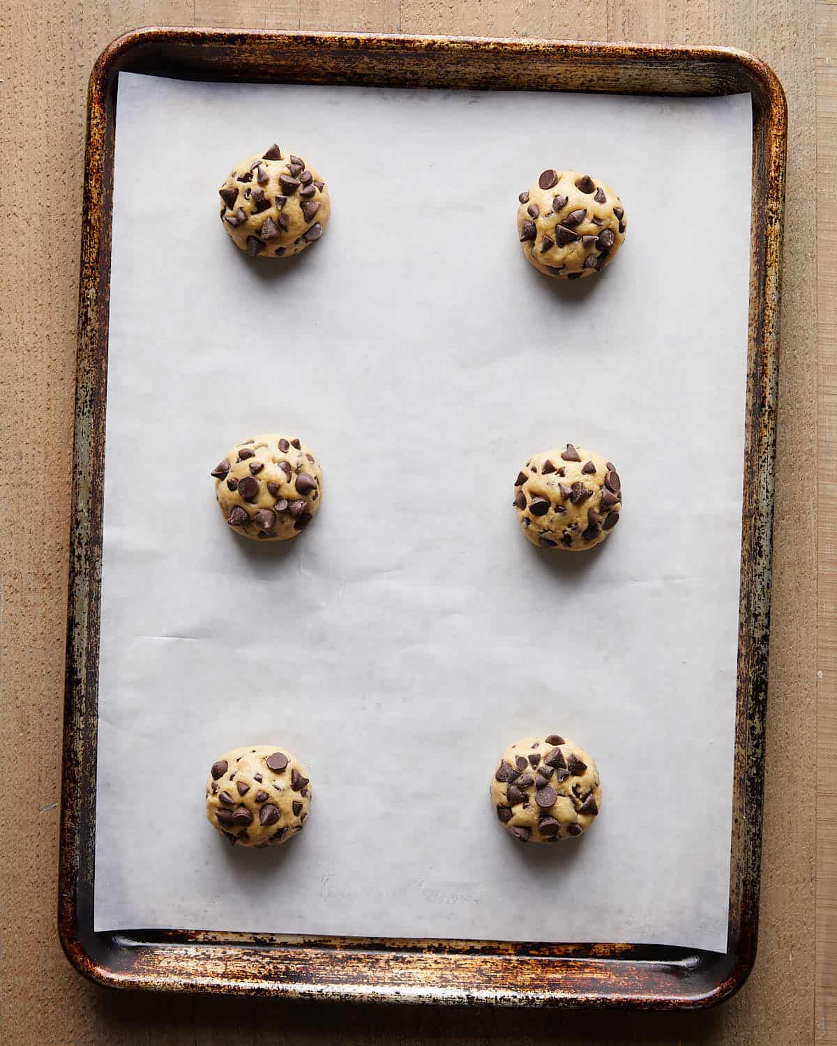 Overhead image of portioned no chill chocolate chip cookie dough placed on a parchment-lined baking sheet, ready to bake for soft, chewy cookies.