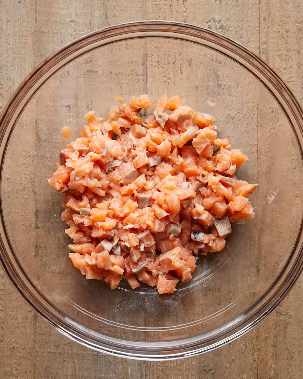 Overhead close-up of finely chopped fresh salmon in a mixing bowl, ready to be mixed for Asian salmon burgers