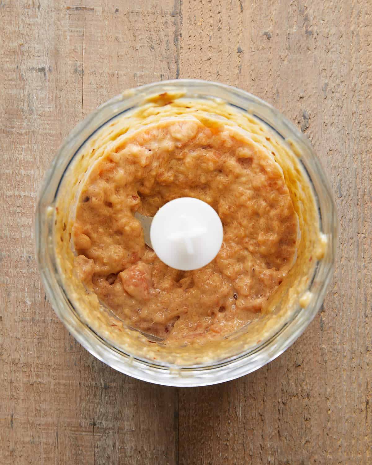 Overhead image of salmon mixture blended into a slightly chunky paste with green onions, garlic, and seasonings—ready to form into Asian salmon burgers for a flavorful, tender texture.