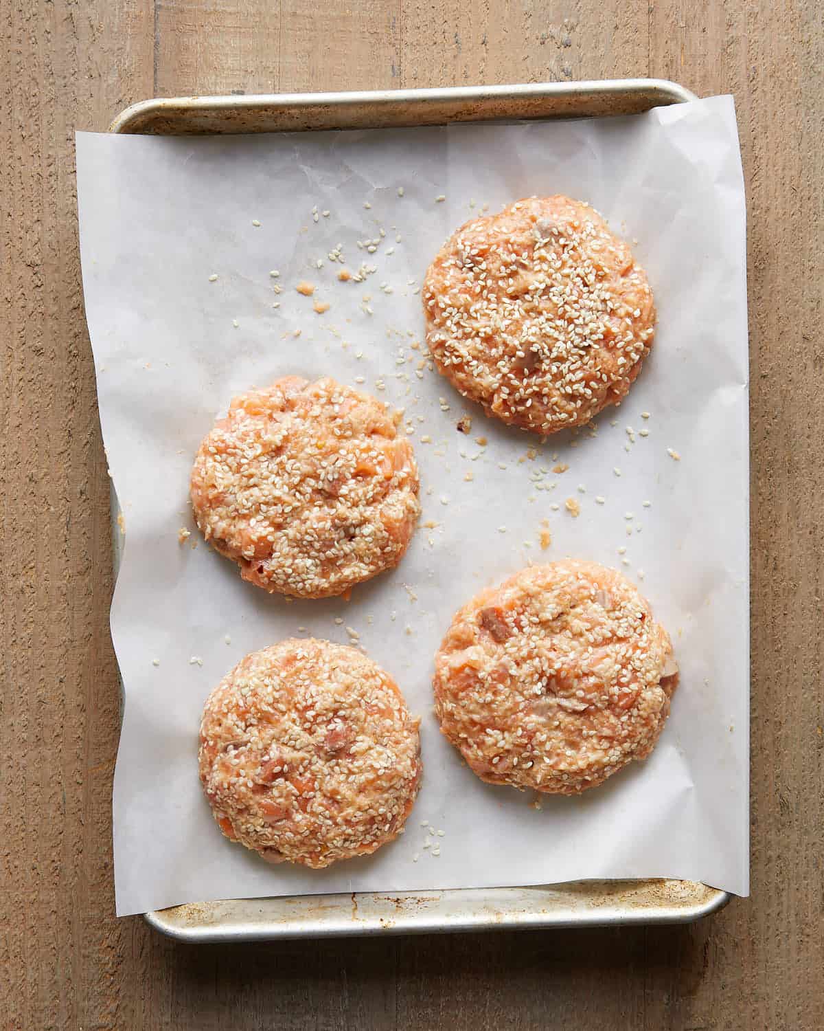Overhead image of formed Asian salmon burger patties arranged on a tray, showing a lightly textured mixture of salmon, herbs, and seasonings ready to cook for flavorful Asian salmon burgers.