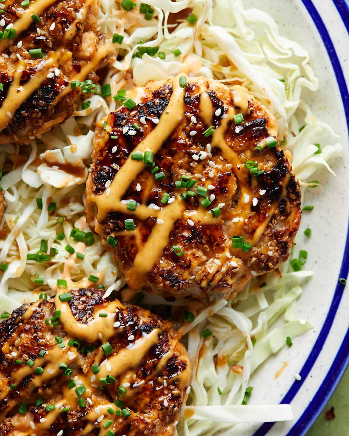 Close-up overhead image of a golden-brown Asian salmon burger patty with visible flakes of salmon, green onions, and sesame.