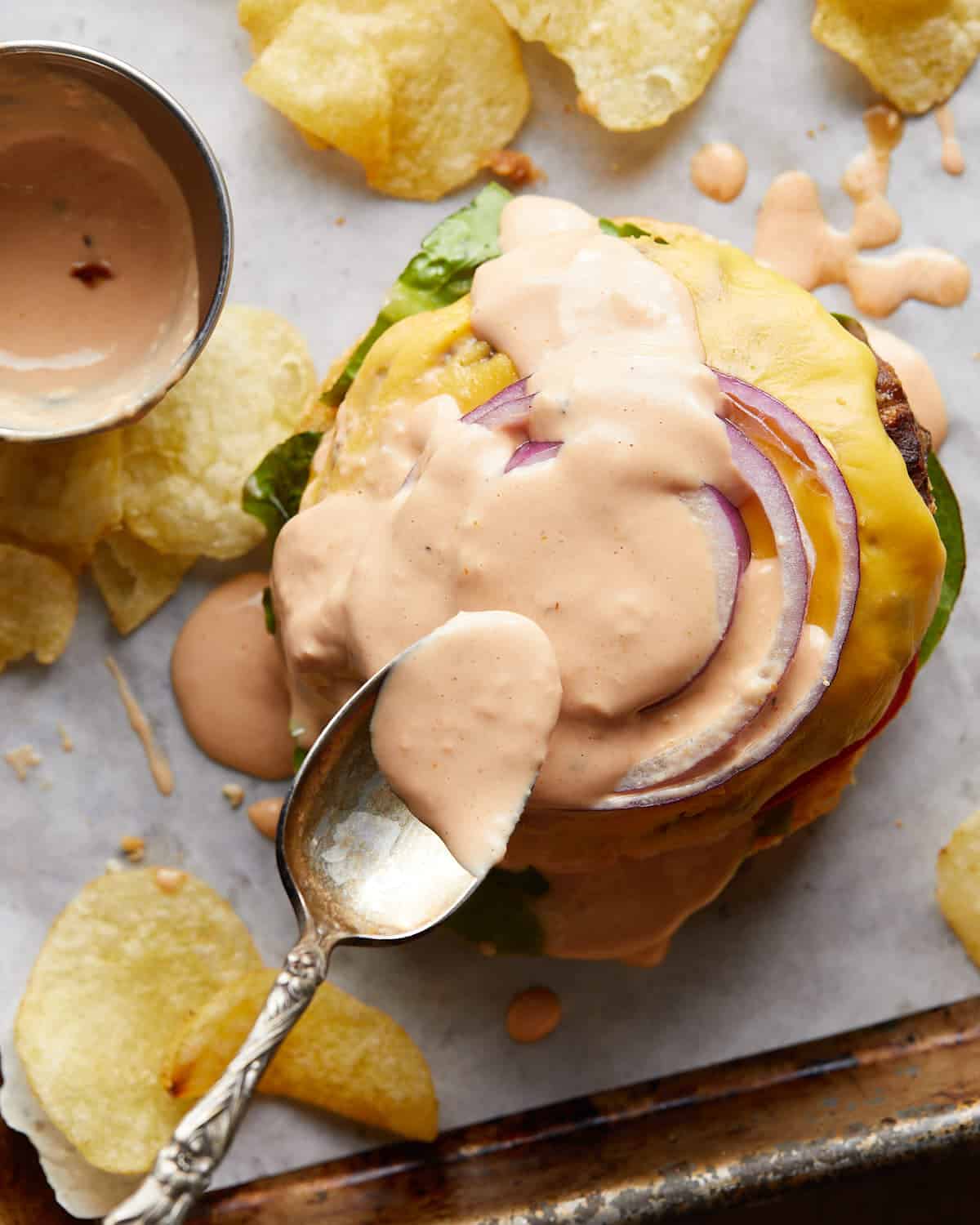 Gold spoon spreading burger sauce onto a burger.