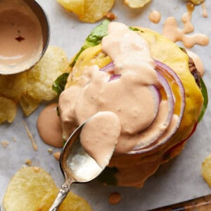 Gold spoon spreading burger sauce onto a burger.