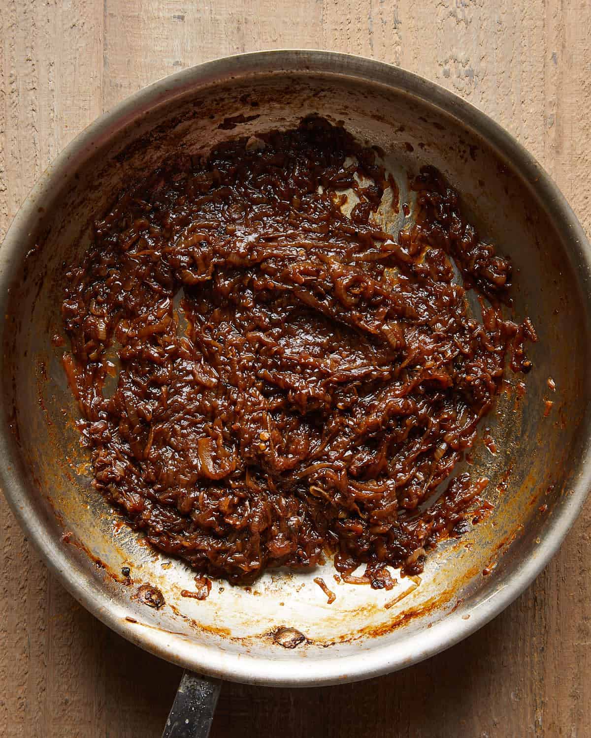 Fully caramelized onions cooked until dark brown and jammy in a pan.