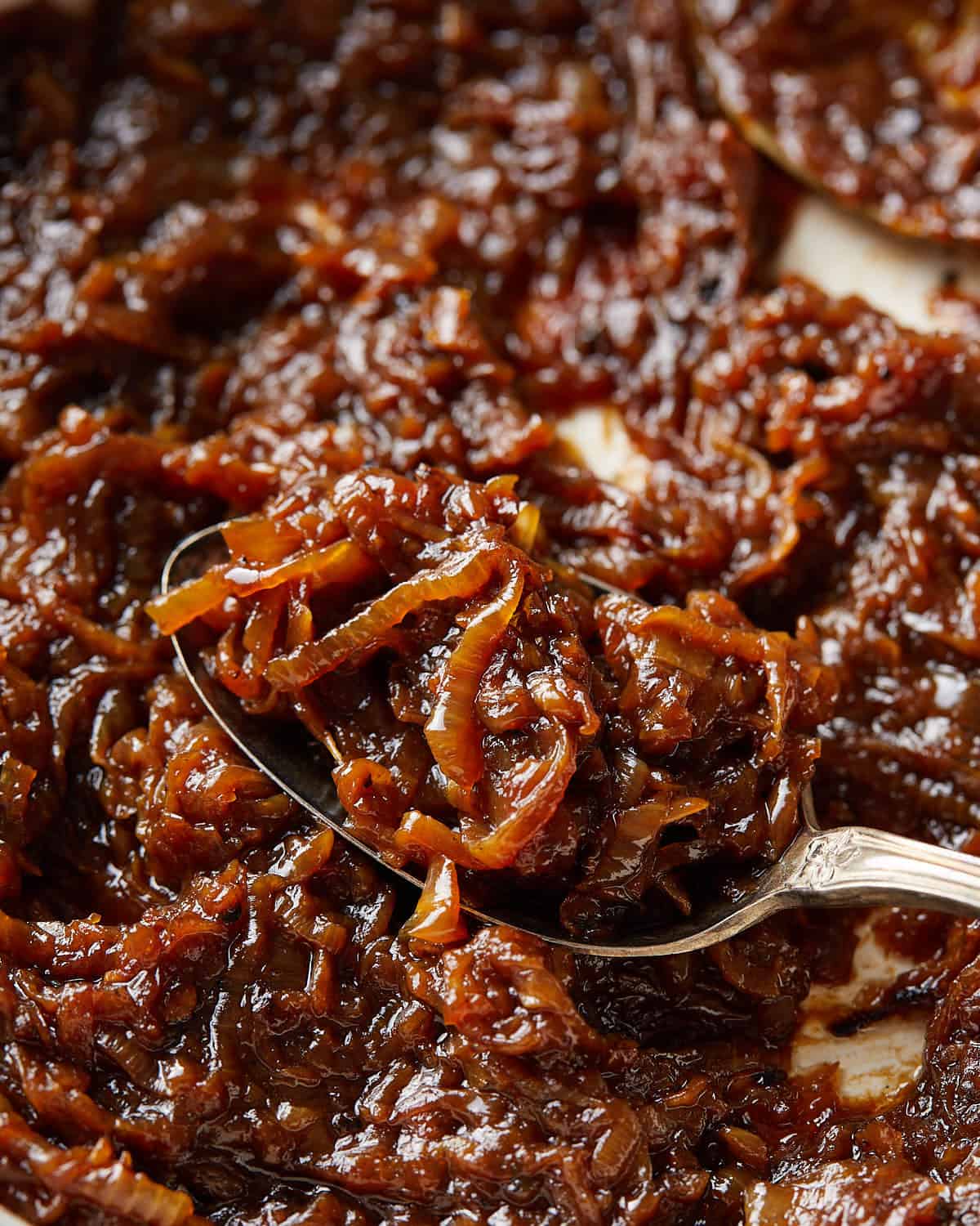Close-up of dark brown caramelized onions with a spoon lifting a bite from the pan.