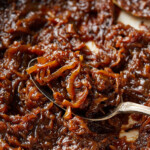 Pan of finished caramelized onions with a spoon resting in the center.