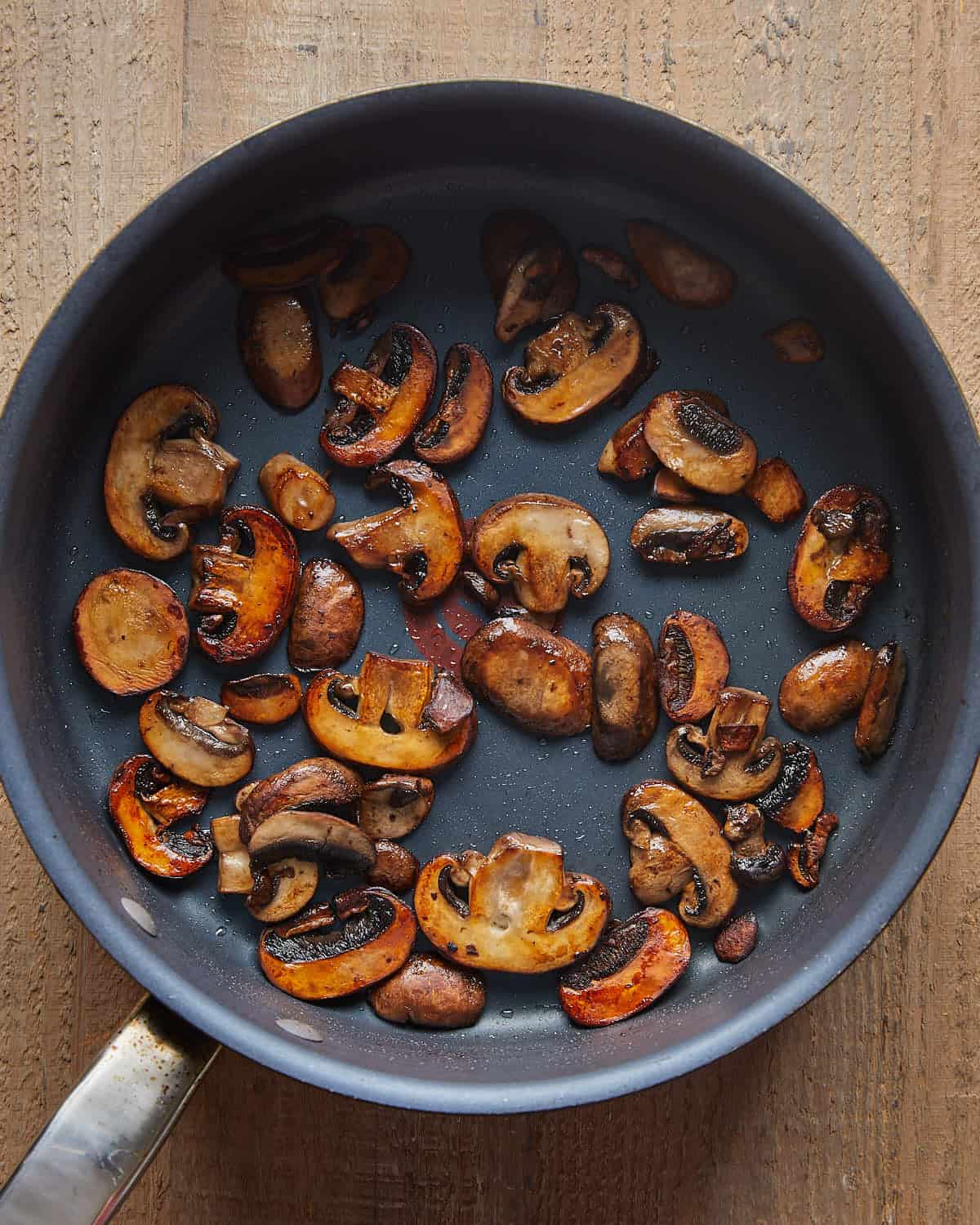 Sliced mushrooms browned in butter in a dark skillet.