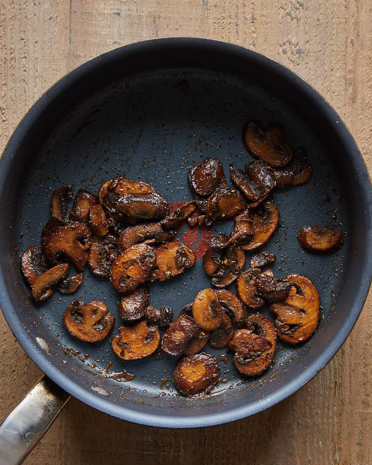 Sliced mushrooms in a skillet after spices, vinegar, and Worcestershire sauce have been added.