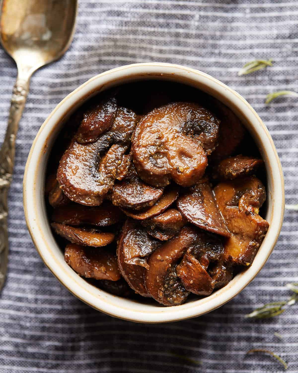 Overhead photo of browned sliced mushrooms in a small bowl on a striped cloth.