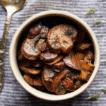 Overhead photo of browned sliced mushrooms in a small bowl on a striped cloth.