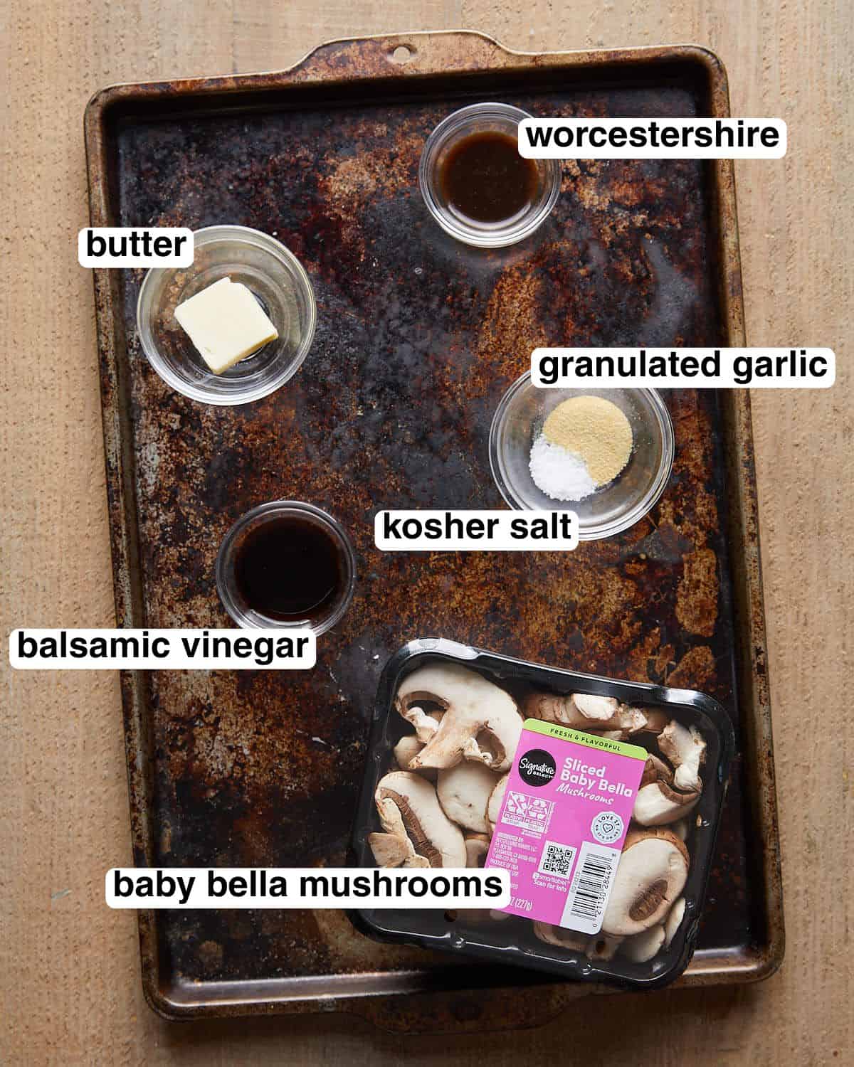 Labeled ingredients for balsamic Worcestershire mushrooms arranged on a sheet pan, including baby bella mushrooms, butter, balsamic vinegar, Worcestershire sauce, kosher salt, and granulated garlic.