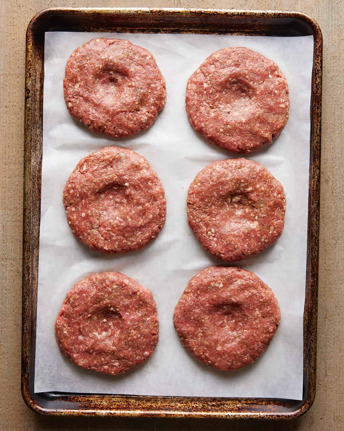 Raw burger patties shaped and arranged on parchment paper.