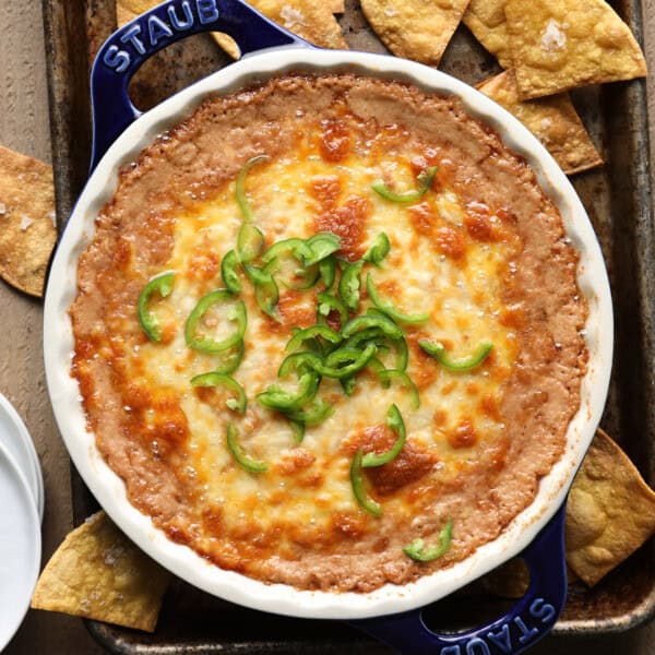 Overhead photo of cheesy bean dip with melted cheese and sliced jalapeños, served with tortilla chips on a blue tray.
