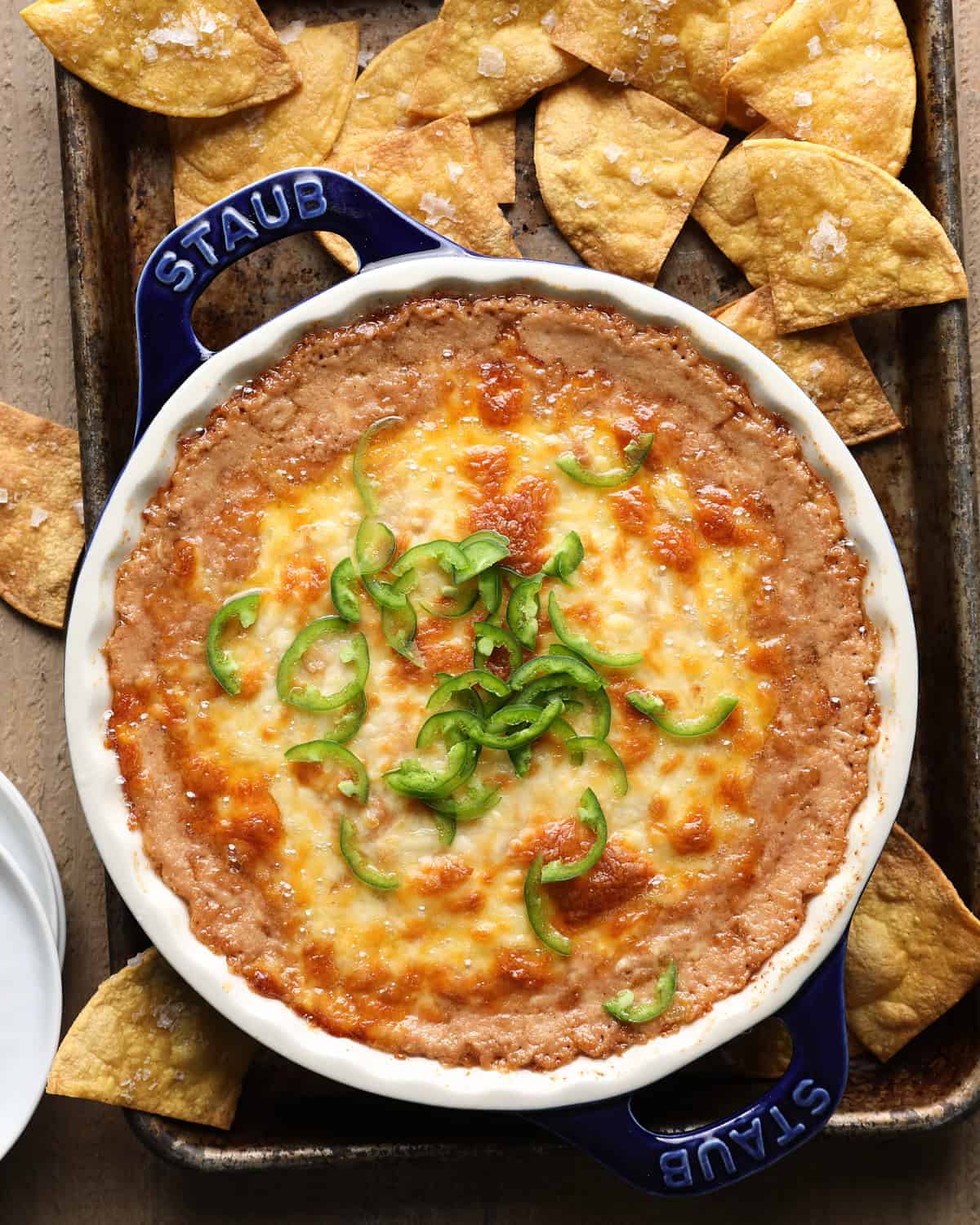 Overhead photo of cheesy bean dip with melted cheese, sliced jalapeños, and tortilla chips.