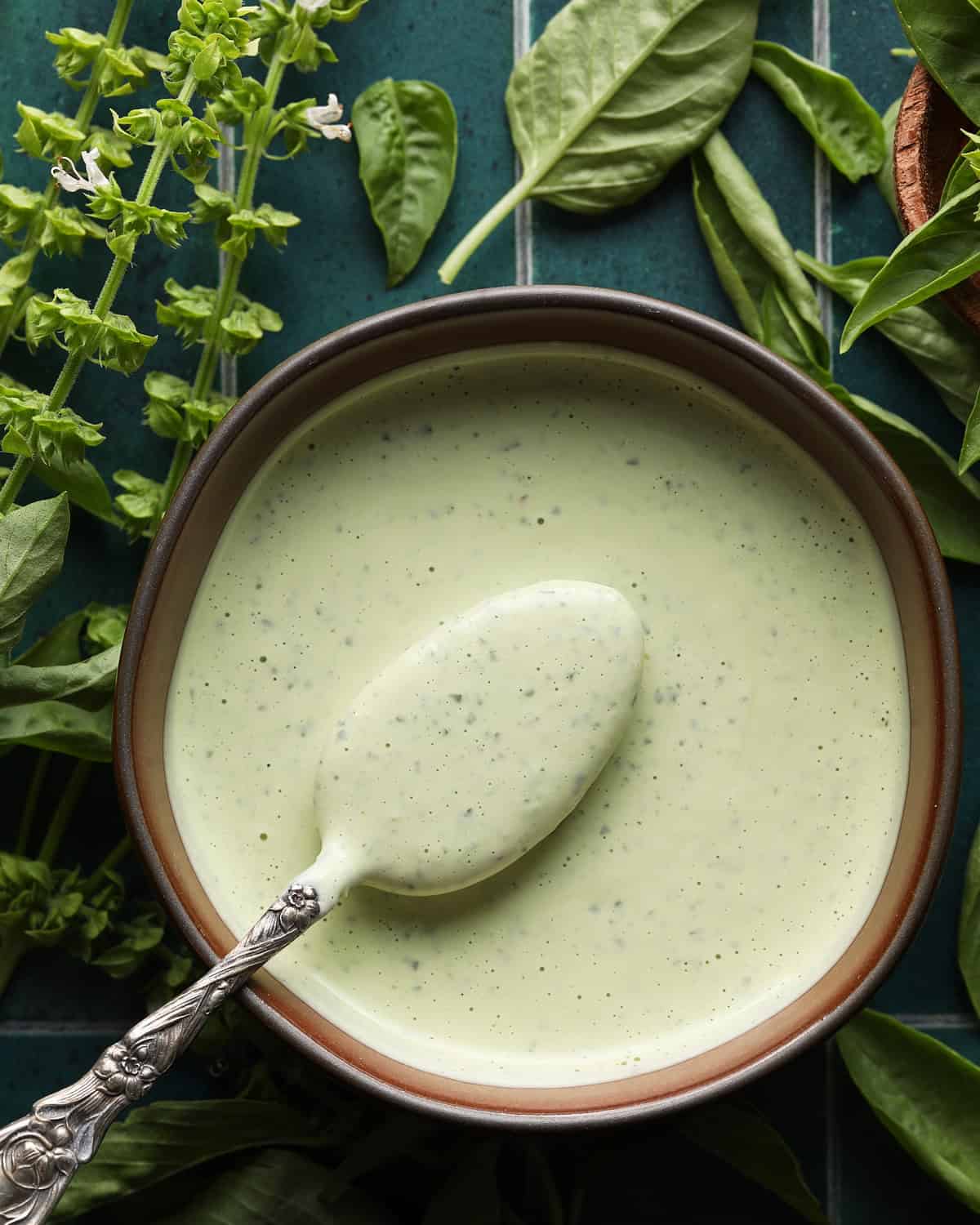 Bowl of creamy basil aioli with a spoon and fresh basil in the background.