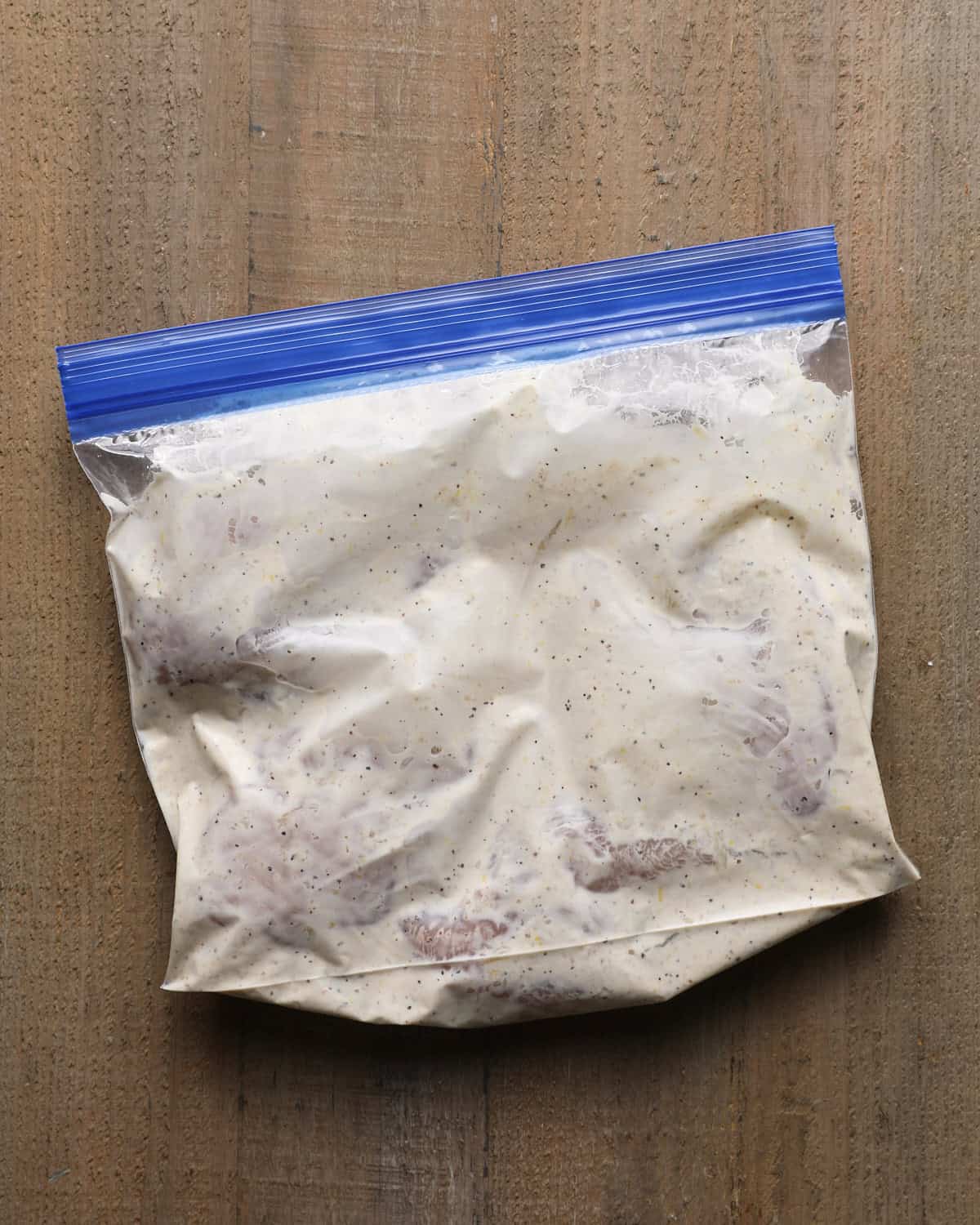 Chicken marinating in Caesar dressing inside a zip-top bag.