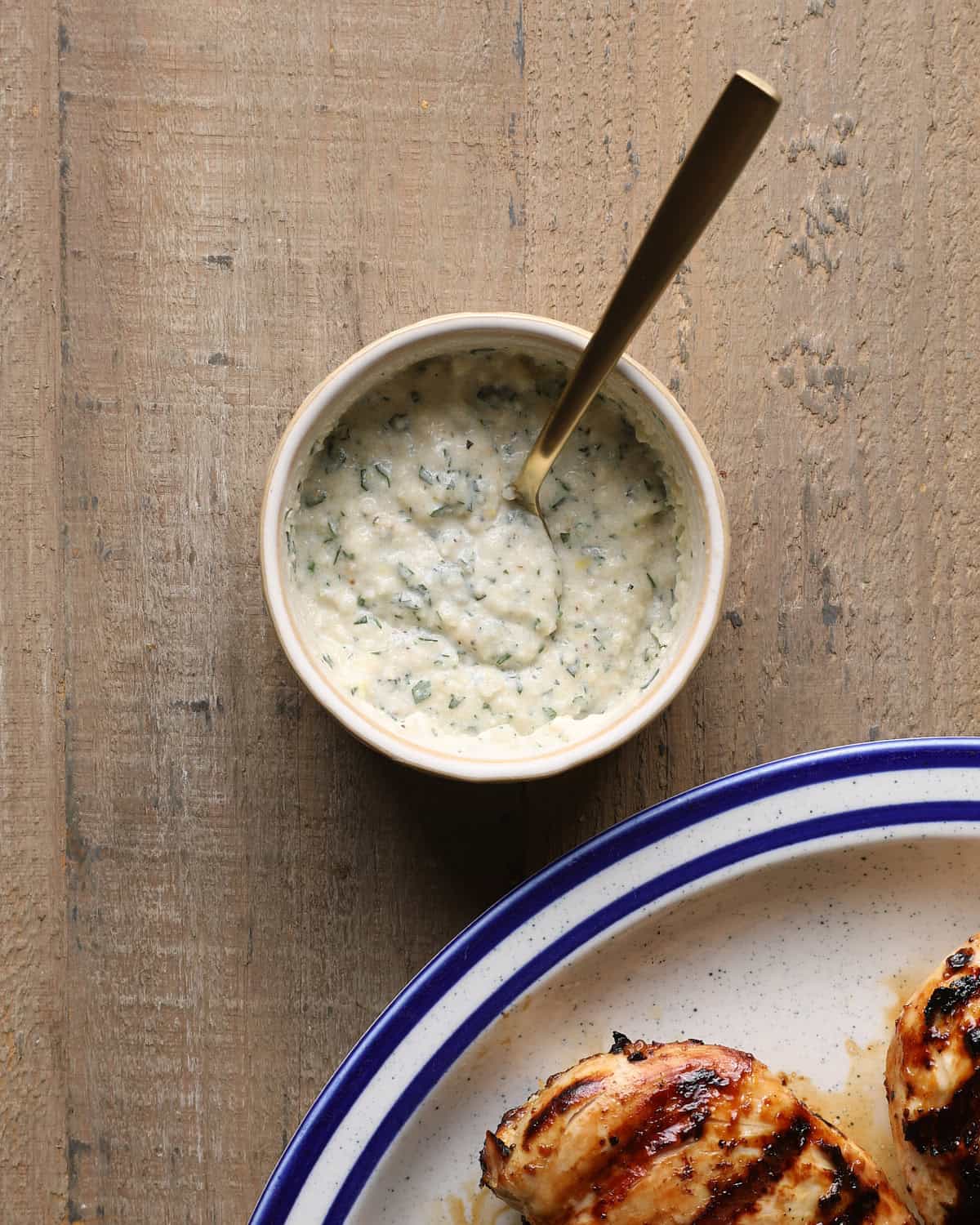 Creamy Caesar finishing sauce in a small bowl with grilled chicken in the background.