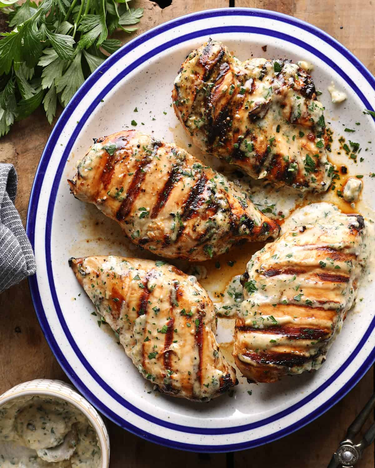Overhead photo of grilled Caesar chicken breasts topped with herbs and served with Caesar sauce.