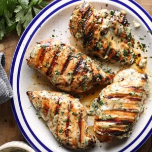 Overhead photo of grilled Caesar chicken breasts topped with herbs and served with Caesar sauce.