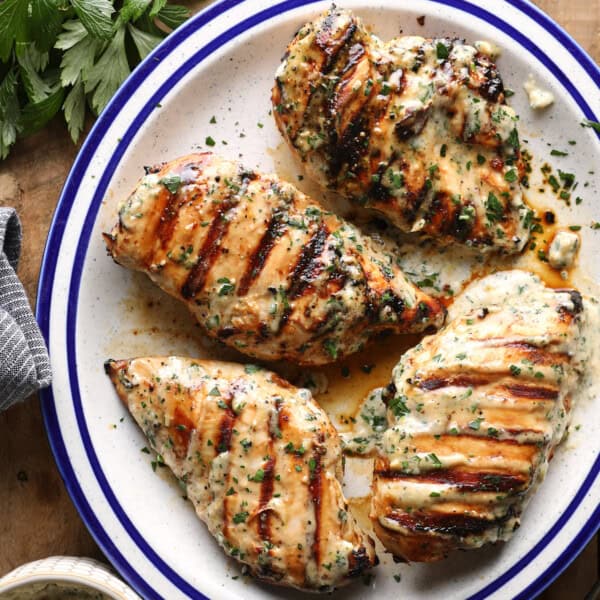 Overhead photo of grilled Caesar chicken breasts topped with herbs and served with Caesar sauce.