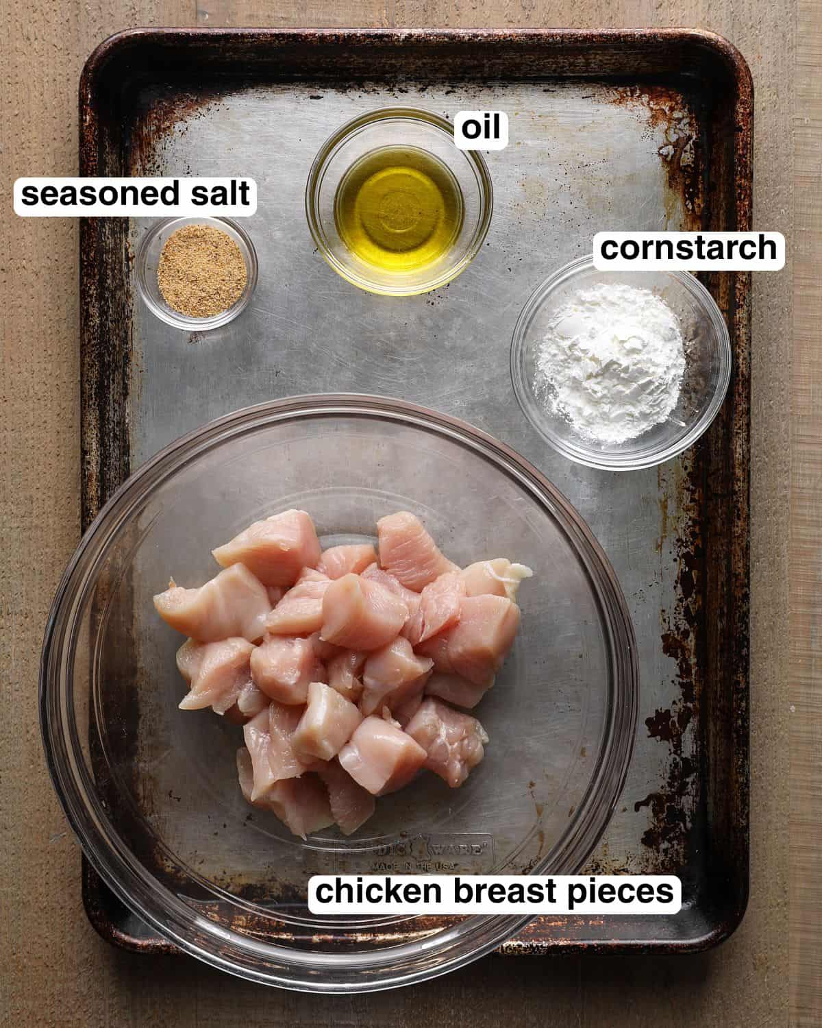 Labeled ingredients for air fryer chicken bites, including chicken breast pieces, seasoned salt, oil, and cornstarch.