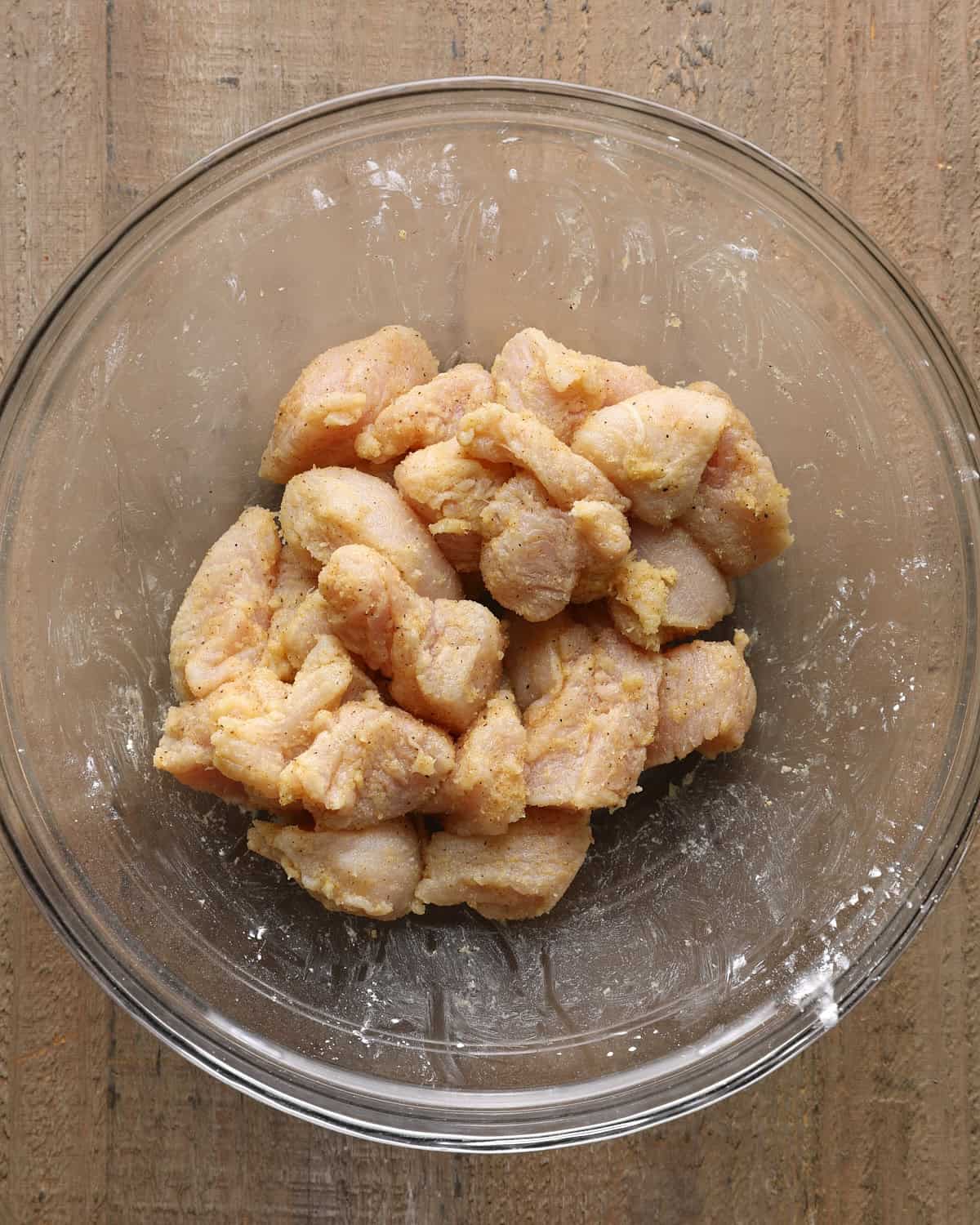 Chicken breast pieces tossed with seasoned salt, cornstarch, and oil in a glass bowl.