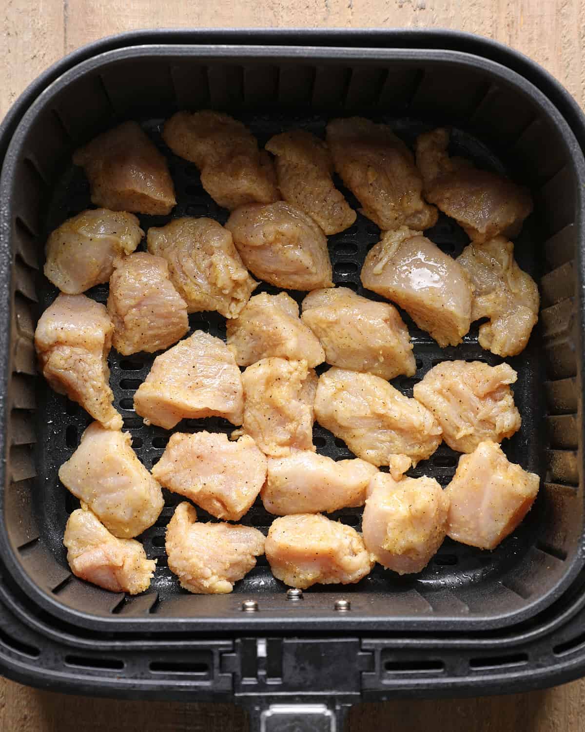 Coated chicken breast pieces arranged in an air fryer basket before cooking.