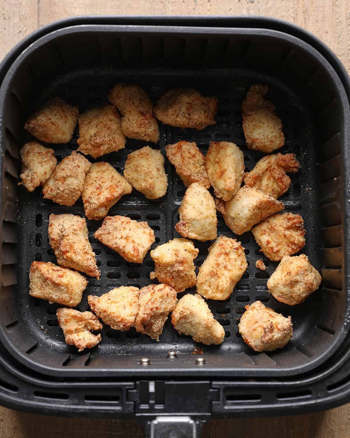 Cooked chicken bites in an air fryer basket after air frying.