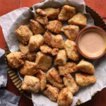 Air fryer chicken bites served in a basket with dipping sauce.